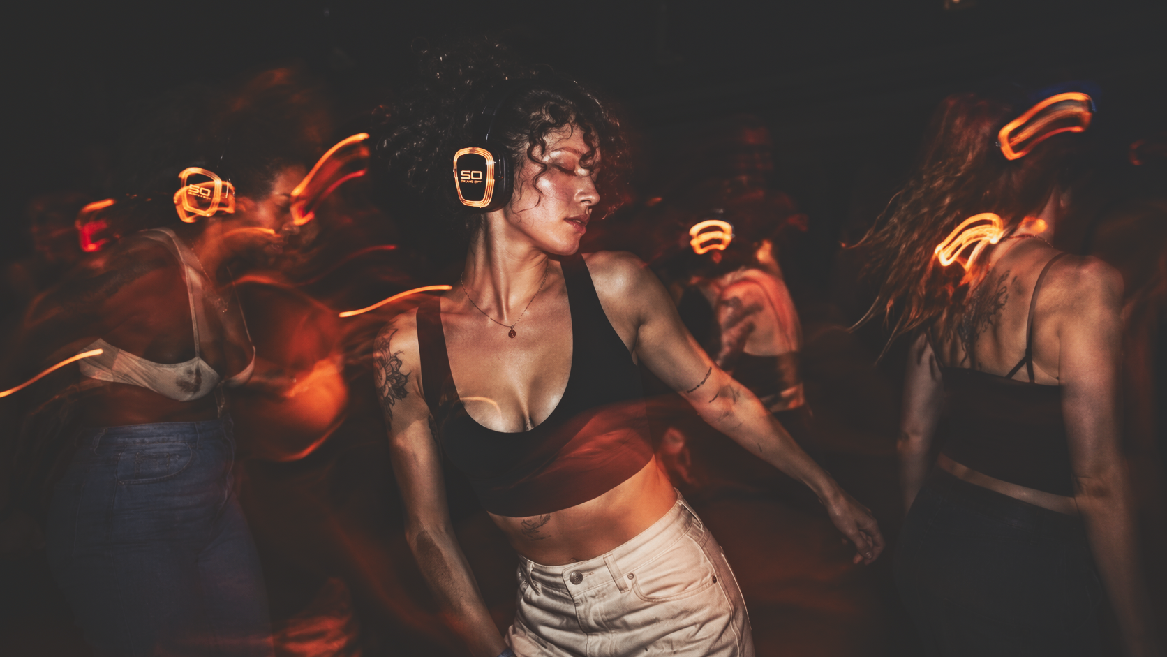 Dancer in Sound Off headphones amid a blurred crowd lit by warm orange light.