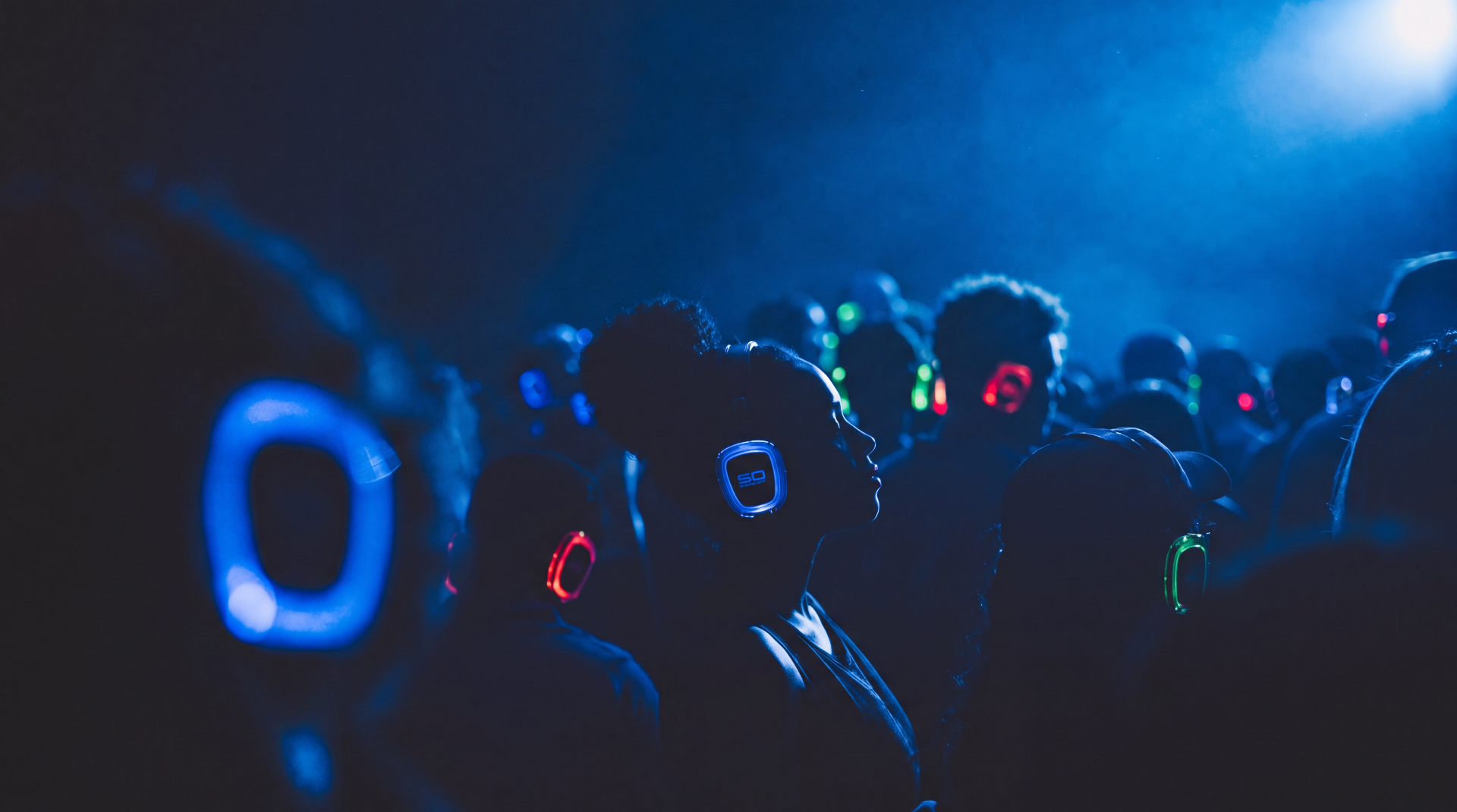 Campus crowd bathed in blue light wearing lit personal-audio headphones.