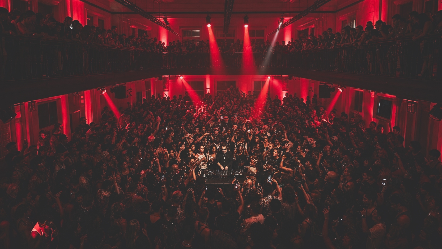 Packed OFFTHERDIIO crowd surrounding a DJ under red stage lighting.